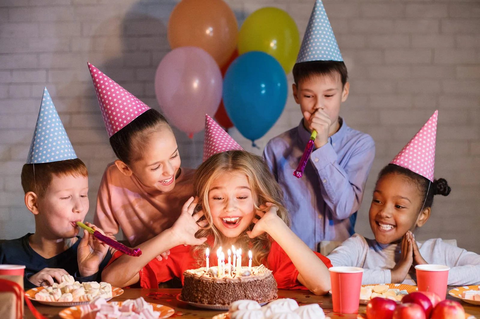 Smiling kids in party hats around a birthday cake with candles