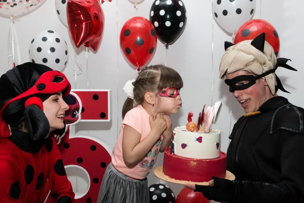 Ladybug and Cat Noir with girl blowing birthday candles